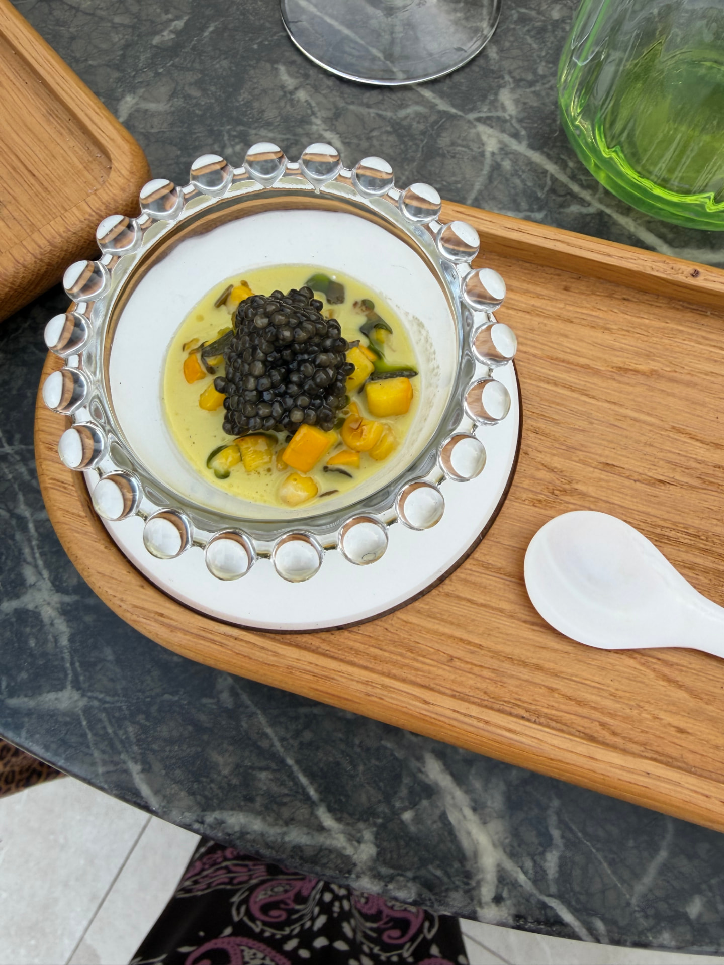 Caviar over a golden corn broth in a beaded glass bowl on a wooden tray at Skina